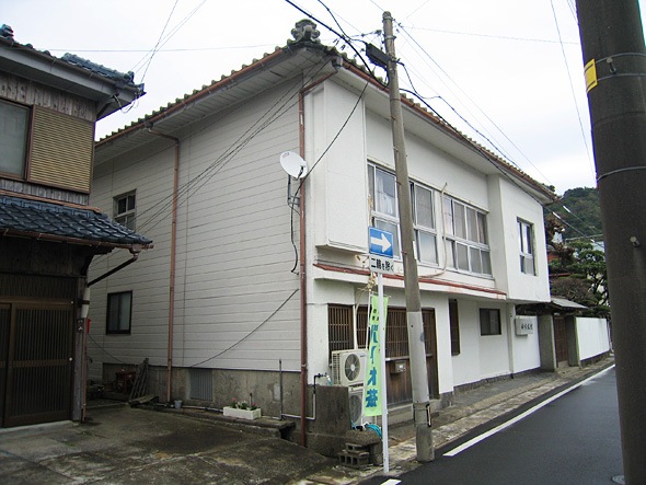 道路に面した白色の木造2階建ての建物の写真