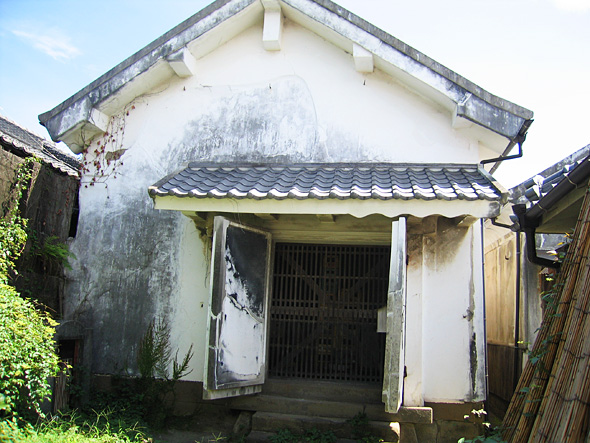 瓦葺の軒下に両開きの厚い漆喰塗りの扉が開いている古い蔵の様子の写真