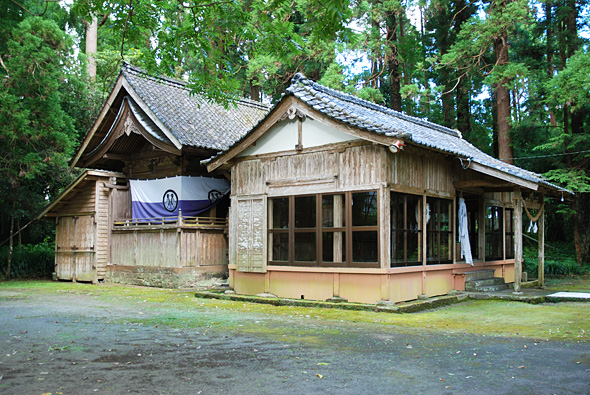 木々の中に建つ、神楽の舞台がある古い神社の写真