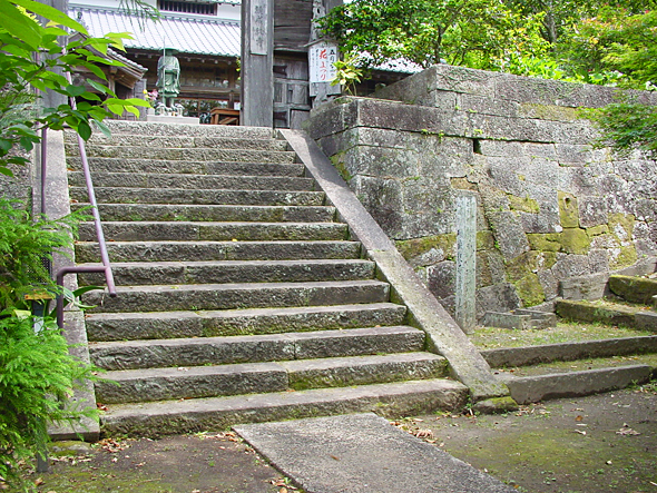 苔むした石垣と古い門へと続く石段の写真