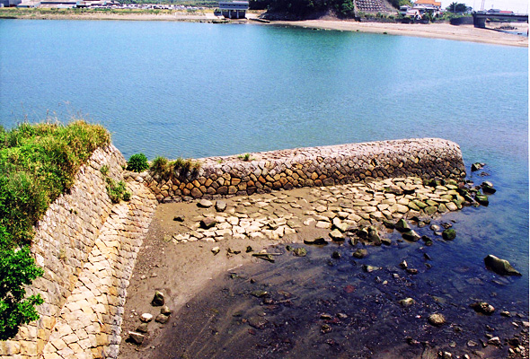 流れる川に向かって伸びる石製の堤の写真