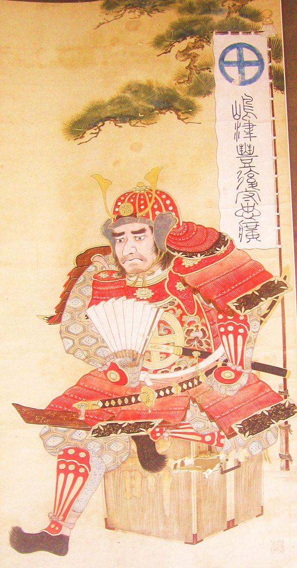 赤い甲冑の武者が扇を持って座っている様子を描いた掛け軸の写真