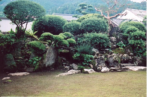 芝生が広がる先に、きれいに剪定された様々な植木が植えられている勝目氏庭園の写真