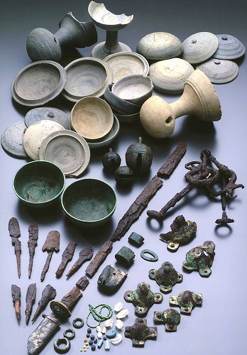 器のような形や装飾品のような形など、様々な色や形をした出土品が種類ごとに並べて置かれている写真