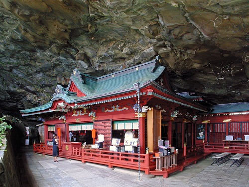 岩屋内に、緑の屋根と朱色の外壁の鵜戸神宮本殿が建っている写真