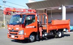 クレーンが装備された赤色のボディの資機材搬送車を右斜め前から撮影した写前