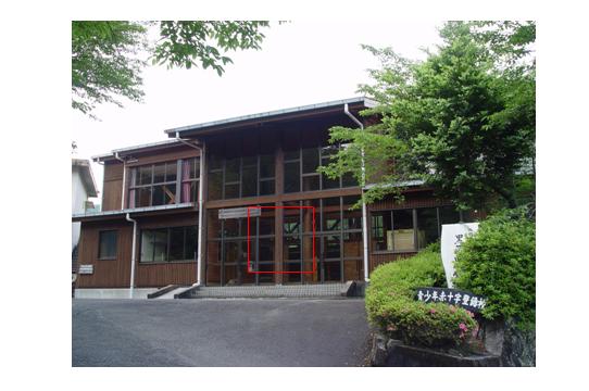 こげ茶色の壁で2階建ての建物中央のガラス張りになっている部分が四角い赤枠で囲まれている旧黒荷田小学校体育館の外観写真