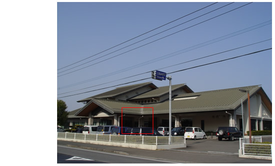周りが白いフェンスで囲まれ、三角屋根をした宮崎県日南保健所全体を写した外観写真の建物中央部分が赤い四角で囲まれている写真