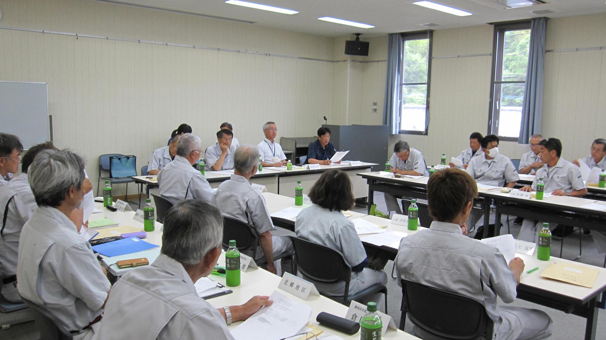 長机を並べて向かい合って座っている関係者たちが会議室に集まって話をしている会議の様子の写真