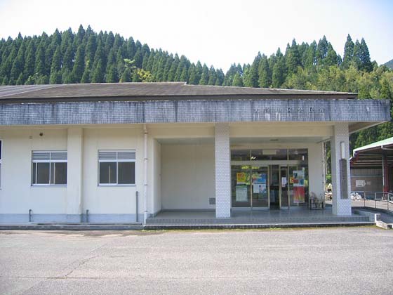 白いコンクリート造りの1階建てで、正面入り口ドアには、張り紙が貼られている日南市立大窪公民館の外観写真