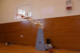 体育館に設置された電動式のバスケットゴール全体を正面右側から写した写真