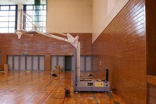 体育館に設置された電動式のバスケットゴール全体を右側から写した写真