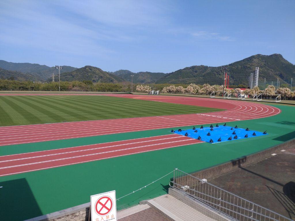 陸上競技場の直線走路の右端に、四角いビニールシートがおかれ、重しで固定されている様子の写真