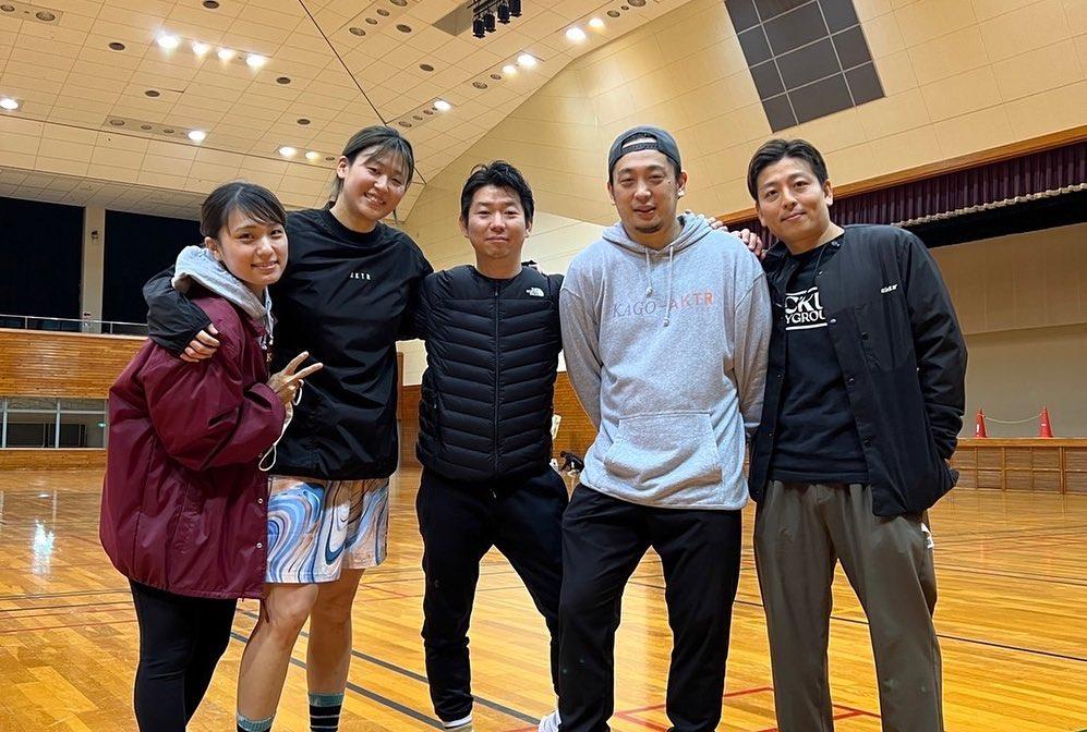 体育館で、丸田氏と男性2名、女性2名が肩を組んで写した記念写真