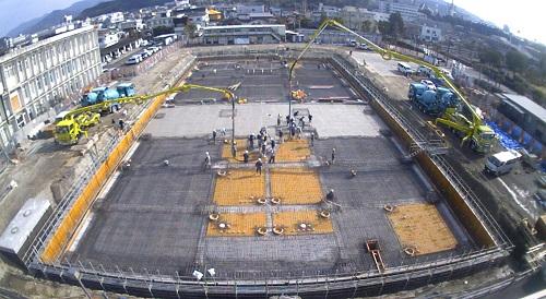 建物の土台となる部分の周りが板のようなもので囲まれ、両側のコンクリートポンプ車から土台部分にコンクリートが流し込まれている写真