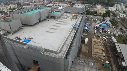 建物全体に足場が組まれ、グレーのネットがされている新庁舎を高い位置から写し、屋上部分が見えている写真