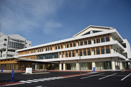 駐車場の奥に、白を基調とした外壁、正面全面に窓ガラスがある3階建ての日南市市役所新庁舎の外観写真