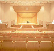 中央にピアノが置いてある舞台があり、木を基調とした観客席が並ぶホールの写真