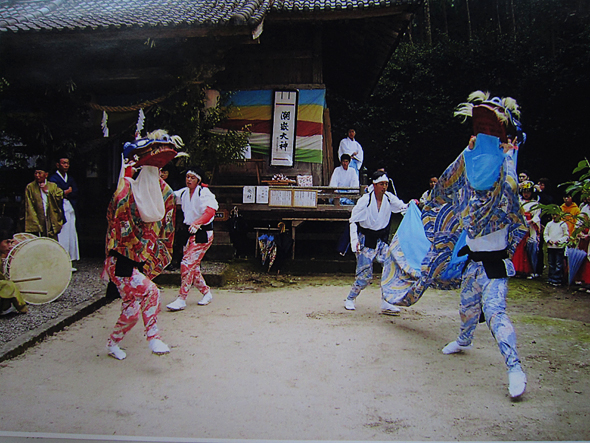 神社の境内で踊る赤い獅子舞と青い獅子舞の写真