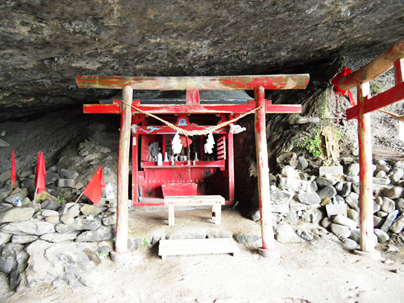 洞窟の中の朱色がはげた鳥居と祀られている小さな祠の写真