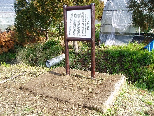 四角に浮き上がった組石の上に「首洗い井戸組石」の看板が設置されている写真