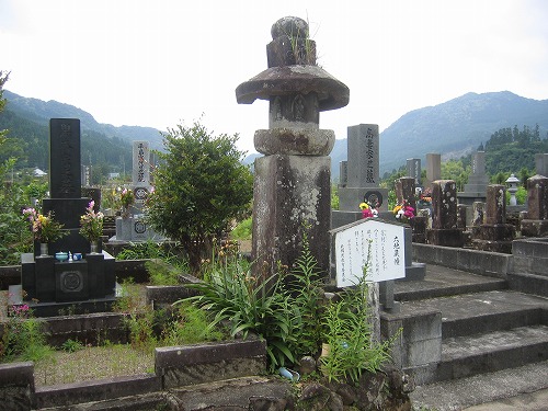 墓地が広がる敷地の一角に、六地蔵幢の説明が記された看板とともに六地蔵幢が設置されている写真