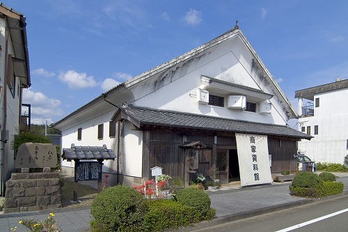白壁に三角屋根の建物で、入り口前には「商家資料館」と書かれた幕が張られている写真