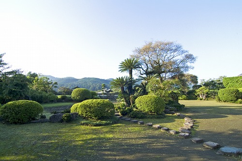 広々とした敷地内にきれいに剪定された様々な種類の植木が並び、芝生上には飛び石が置かれている豫章館庭園の写真