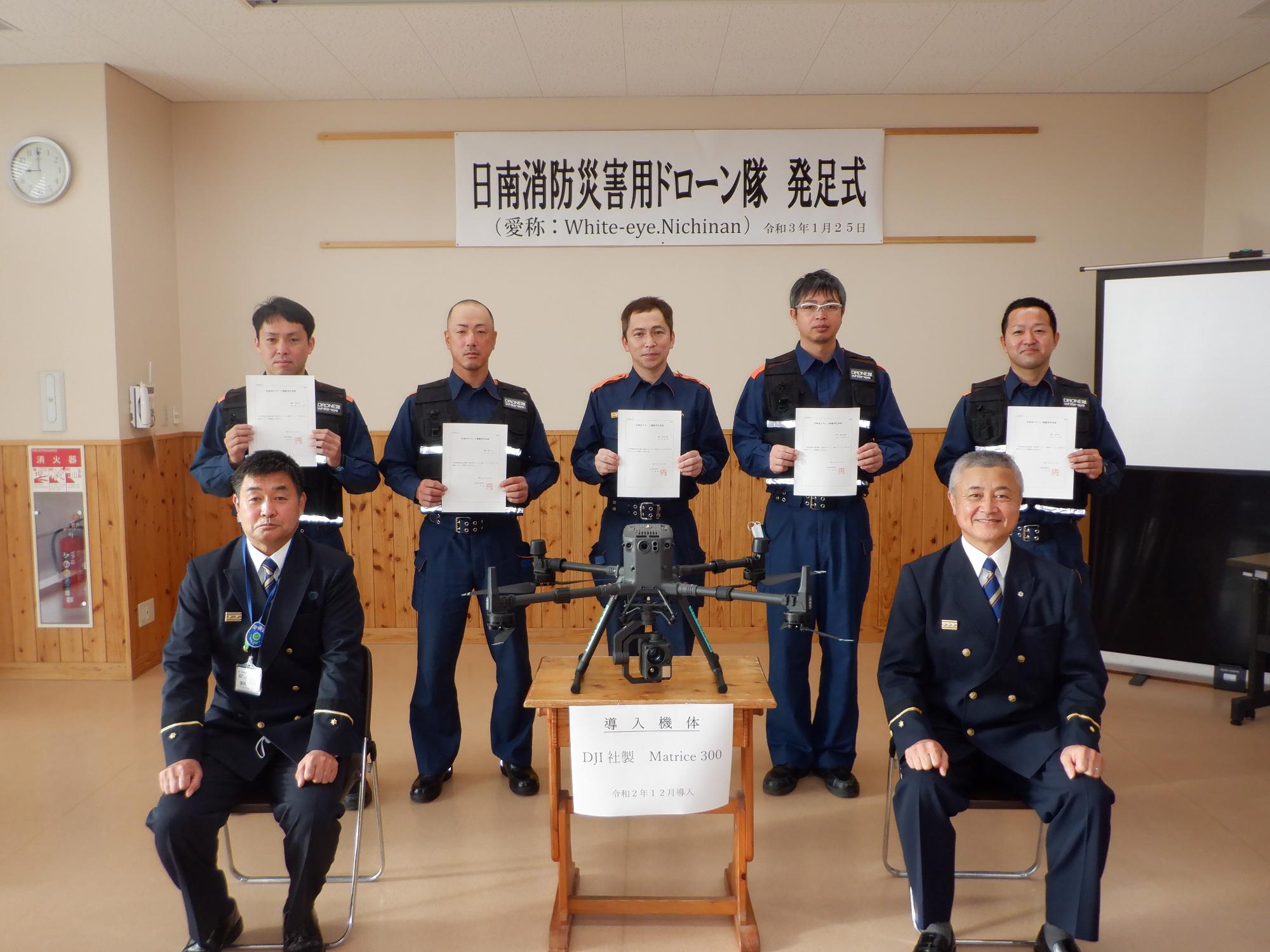 ドローン隊発足式の画像です。7人の消防職員が写っています。後ろに5名、前に2名います。後ろの2名は認定書を持っています。