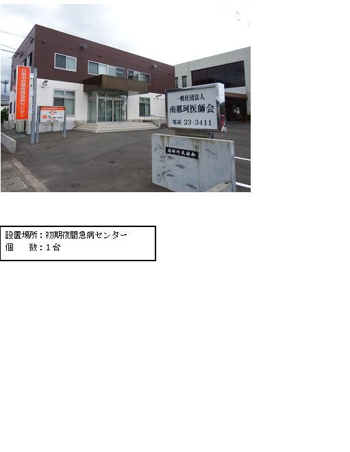 上段：敷地内入口部分に「一般社団法人南那珂医師会」と書かれた看板が設置され、敷地内に1階部分が白、2階部分が茶色の外壁で2階建ての四角い建物があり、建物横には「日南市初期夜間急病センター」と書かれたオレンジ色の看板が立っている施設の外観写真 下段：「設置場所：初期夜間急病センター 個数：1台」と書かれた案内文