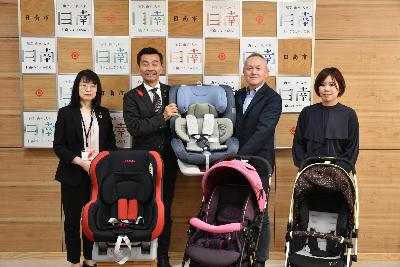 左から健康福祉部長、日南市長、南郷包装社長、サガリオ社長がベビーカー2台とチャイルドシート2台と一緒に写っている写真