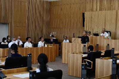 議場に小学生と中学生の代表が集まり、小学生の男の子が壇上から市長や副市長等に対して質問を行っている写真