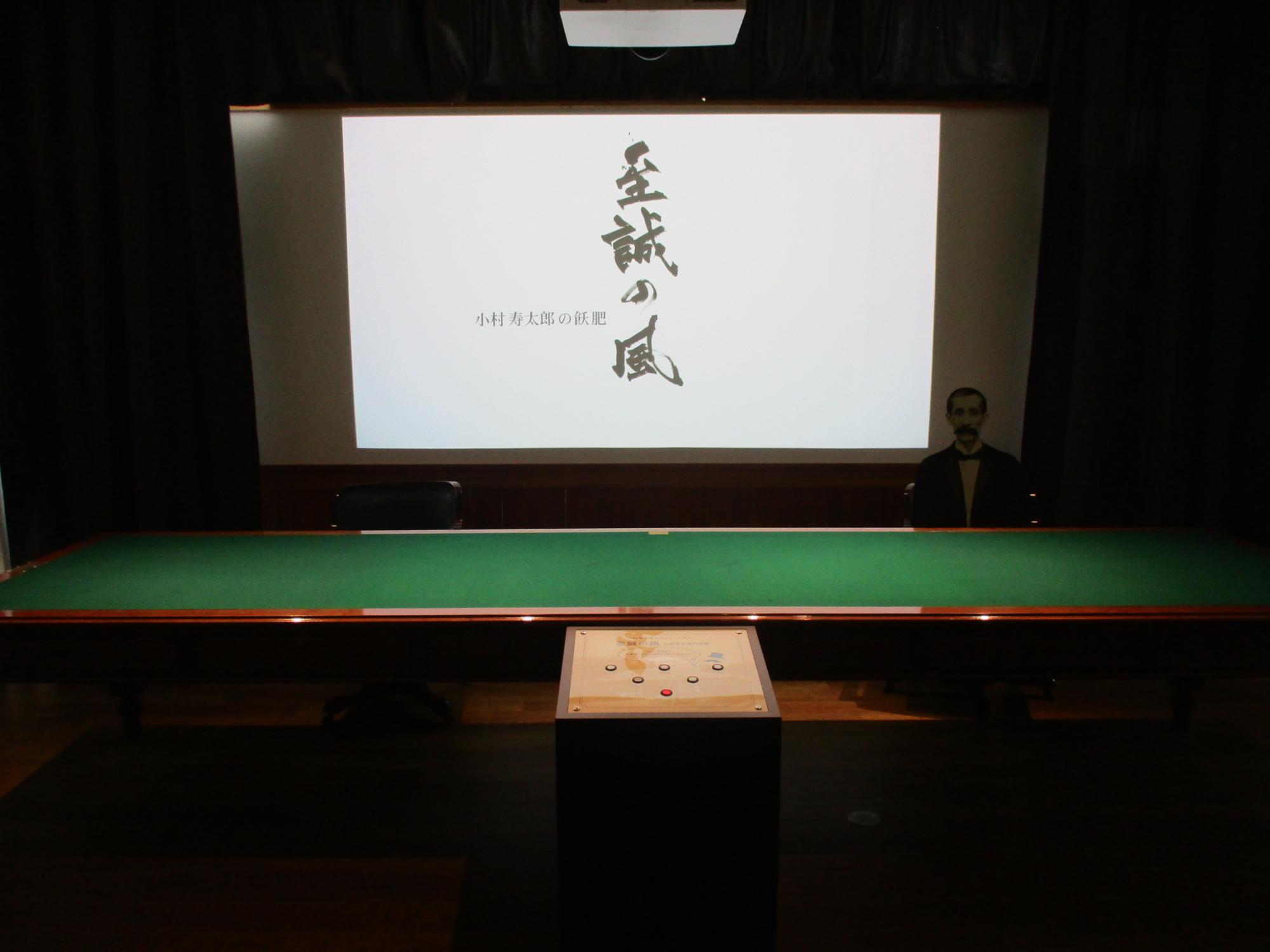 日露講和条約調印時の机（復元レプリカ）と小村寿太郎の映像が映る写真