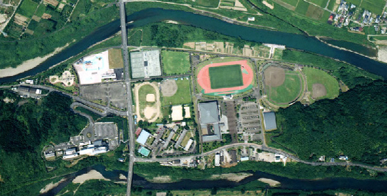 川のそばにあり、陸上競技場、球場、ドームなどが集合している、日南総合運動公園を上空から撮影した写真