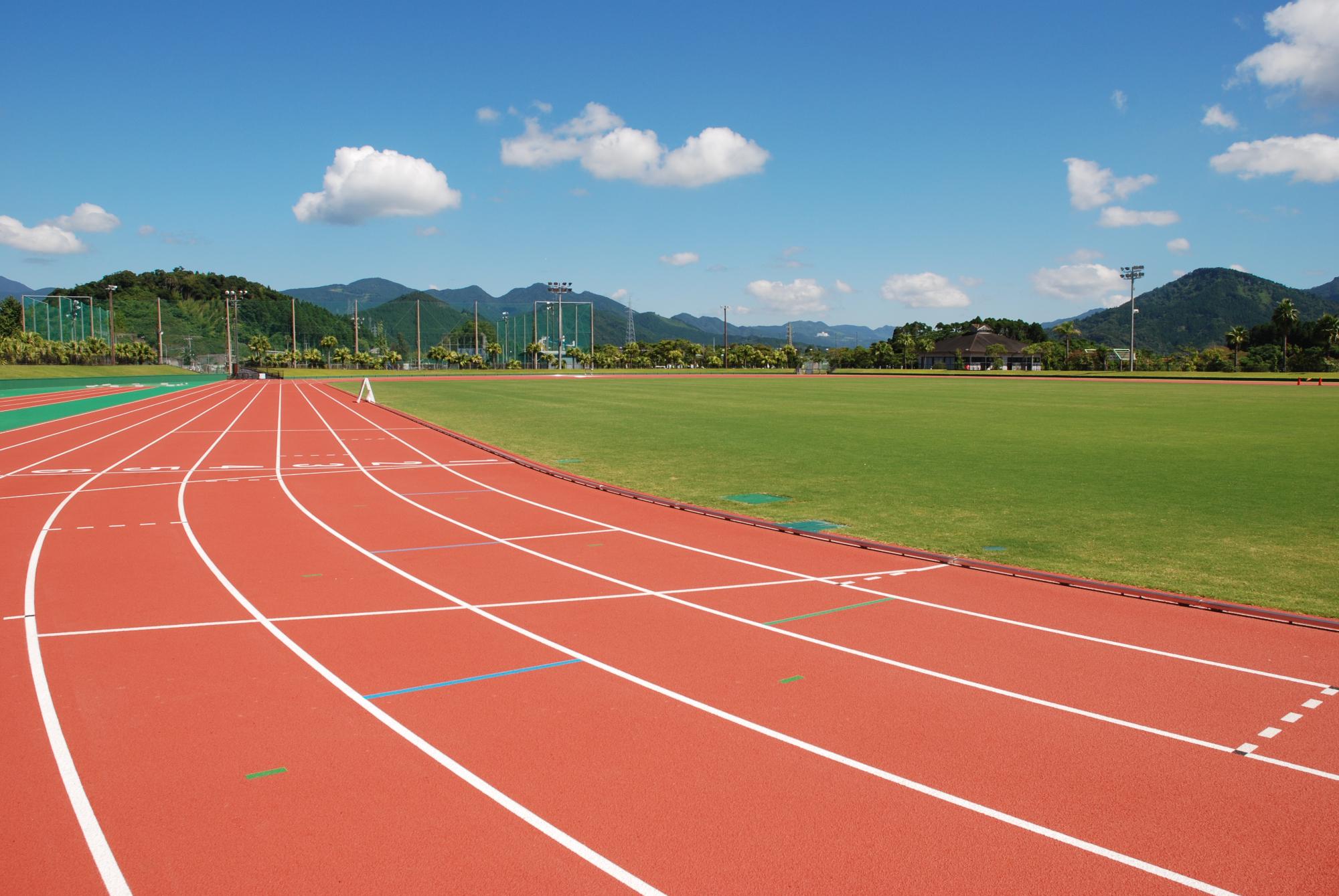 奥に野球場と山並みが見える陸上競技場のトラックを近くから写した写真